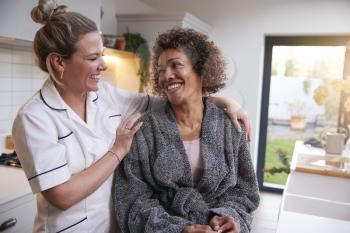Mature Woman In Dressing Gown Talking With Female Nurse In Kitchen At Home