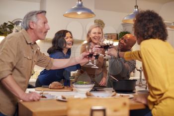 Group Of Mature Friends Making A Toast As They Meet At Home For Meal And Serve Food In Kitchen