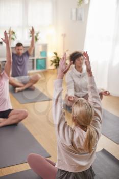 Group With Teacher Sitting On Exercise Mats Stretching In Yoga Class Inside Community Center
