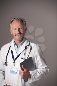 Studio Portrait Of Mature Male Doctor In White Coat Using Digital Tablet Against Grey Background