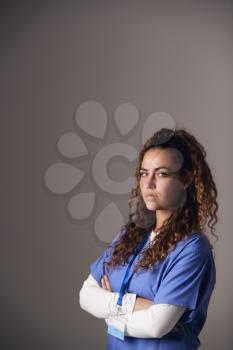 Studio Portrait Of Young Female Nurse Wearing Scrubs Standing Against Grey Background
