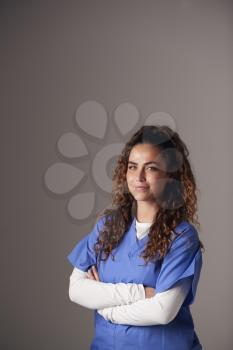 Studio Portrait Of Young Female Nurse Wearing Scrubs Standing Against Grey Background