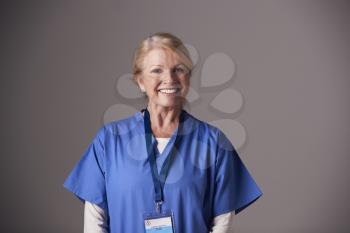 Studio Portrait Of Mature Female Nurse Wearing Scrubs Standing Against Grey Background