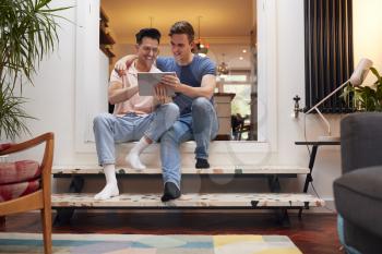 Loving Same Sex Male Couple Using Digital Tablet As They Relax At Home Together