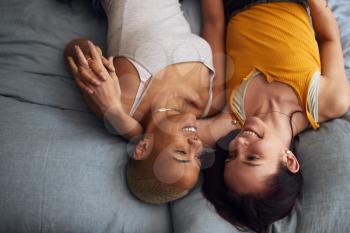 Overhead Shot Of Loving Same Sex Female Couple Lying On Bed At Home Holding Hands Together