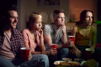 Group Of Friends With Drinks Sitting On Sofa At Home Watching Horror Movie Together