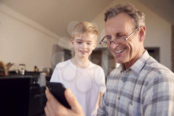 Grandson Showing Grandfather How To Solve Problem And Use Mobile Phone At Home