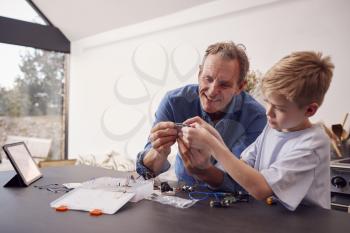 Grandson With Grandfather Assembling Electronic Components To Build Robot Together At Home