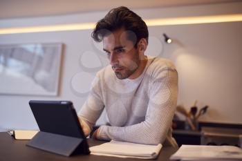 Man In Kitchen Working Or Studying From Home Using Digital Tablet