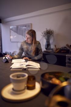 Evening Shot Of Woman In Kitchen Working Or Studying From Home Using Digital Tablet