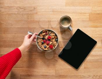 Overhead Flat Lay Of Woman Using Digital Tablet On Table Laid For Breakfast With Cereal And Coffee