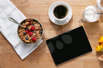 Overhead Flat Lay Of Digital Tablet On Table Laid For Breakfast With Cereal And Coffee
