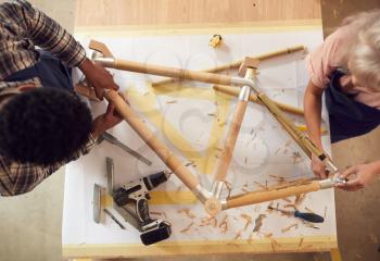 Overhead View Of Multi-Cultural Team In Workshop Assembling Hand Built Bamboo Bicycle Frame
