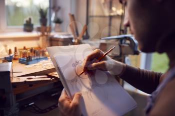 Close Up Of Male Jeweller Sketching Out Design For Ring In Studio