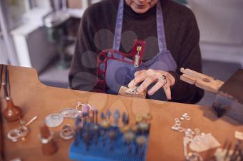 Close Up Of Female Jeweller Working On Piece With Saw In Studio