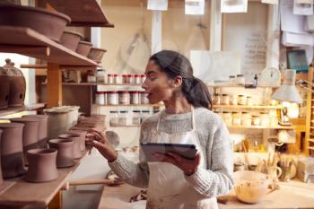 Female Potter In Ceramics Studio Checking Orders Using Digital Tablet