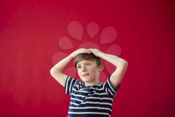Portrait Of Smiling Boy With Hands On Head Against Red Studio Background