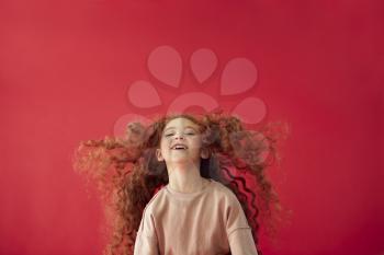 Portrait Of Girl With Long Red Hair Jumping In Air Against Red Studio Background Smiling At Camera