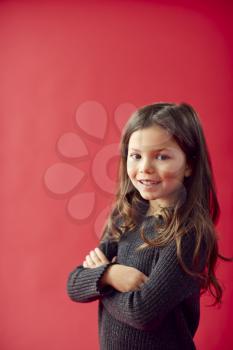Portrait Of Young Girl With Folded Arms Against Red Studio Background Smiling At Camera