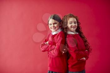 Two Elementary School Pupils Wearing Uniform Back To Back Against Red Studio Background
