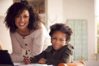 Portrait Of Mother Helping Son With Homework Sitting At Kitchen Counter Using Digital Tablet
