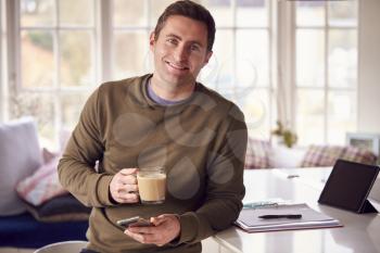 Portrait Of Man With Digital Tablet Working From Home On Kitchen Counter Drinking Coffee