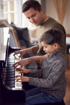 Young Boy Learning To Play Piano Having Lesson From Male Teacher