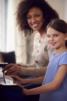 Portrait Of Young Girl Learning To Play Piano Having Lesson From Female Teacher