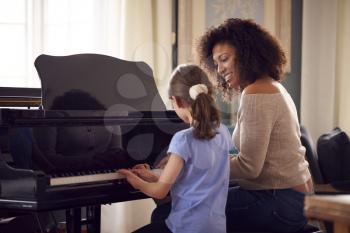 Young Girl Learning To Play Piano Having Lesson From Female Teacher