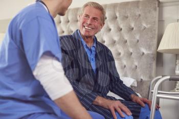 Male Doctor Making Home Visit To Senior Man With Walking Frame For Medical Check In Bedroom