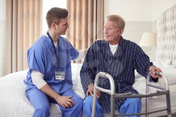 Male Doctor Making Home Visit To Senior Man With Walking Frame For Medical Check In Bedroom