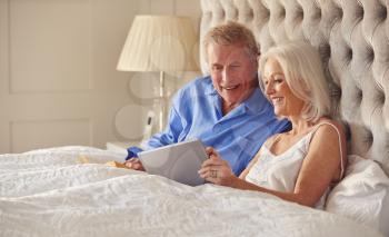 Senior Couple At Home In Bed Self Isolating Using Digital Tablet During Covid 19 Lockdown