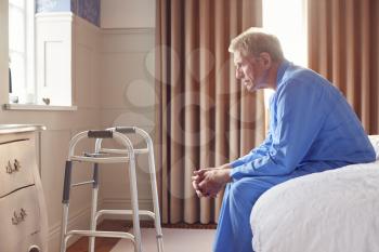 Unhappy And Depressed Senior Man Sitting On Edge Of Bed At Home During Lockdown For Covid-19