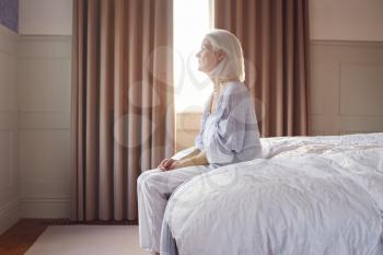 Unhappy And Depressed Senior Woman Sitting On Edge Of Bed At Home