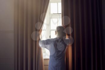 Senior Woman In Bedroom Opening Curtains In The Morning