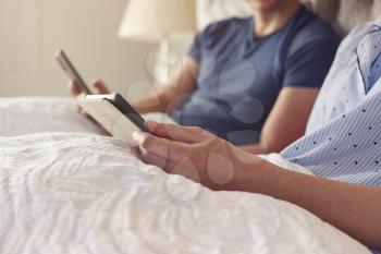 Close Up Of Couple At Home In Bed Using Digital Tablet And Mobile Phone During Covid 19 Lockdown