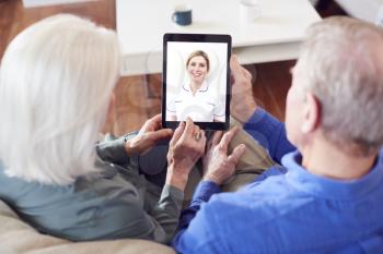 Female Doctor Having Video Consultation With Senior Couple On Digital Tablet At Home
