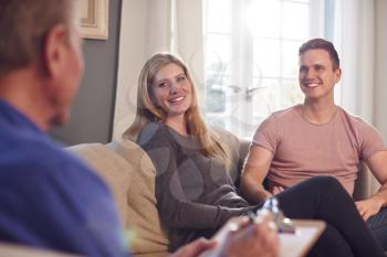 Male Social Worker With Clipboard Visiting Young Couple At Home