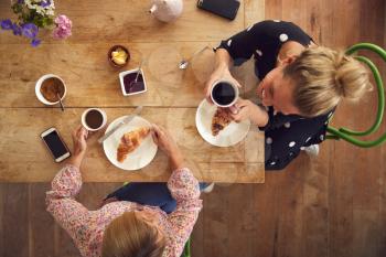 Overhead View Of Two Female Friends In Coffee Shop Meeting Up In Socially Distanced Way