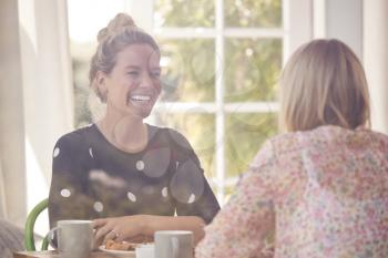 Two Female Friends In Coffee Shop Meeting Up In Socially Distanced Way Viewed Through Window