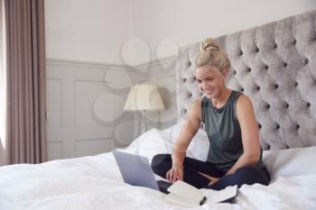 Businesswoman Sitting On Bed With Laptop Working From Home On Video Call During Pandemic Lockdown
