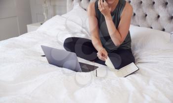 Close Up Of Businesswoman Sitting On Bed With Laptop And Mobile Phone Working From Home
