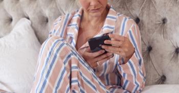 Woman In Pyjamas Sitting On Bed With Mobile Phone Checking Messages