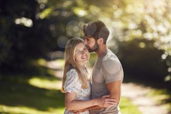 Loving Couple Hugging As They Walk Along Countryside Path In Summer Together