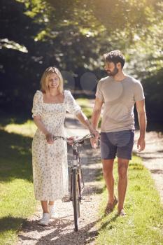 Couple Walking Along Summer Countryside Path Pushing Bike