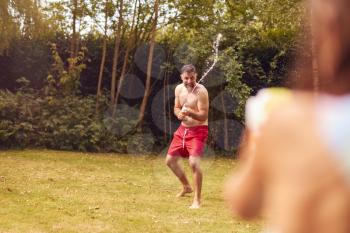 Father And Son Wearing Swimming Costumes Having Water Fight With Water Pistols In Summer Garden