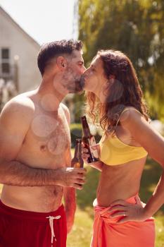 Loving Couple Wearing Swimming Costumes Standing In Pool In Summer Garden At Home Drinking Beer