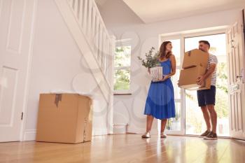 Mature Couple Carrying Boxes Through Front Door Into New Home On Moving Day