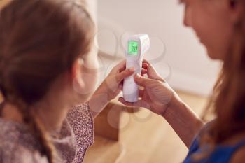 Close Up Of Mother Checking Daughters Temperature At Home Using Contactless Digital Thermometer
