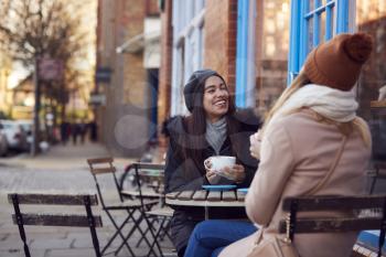 Two Female Friends Meeting Sitting Outside Coffee Shop On City High Street